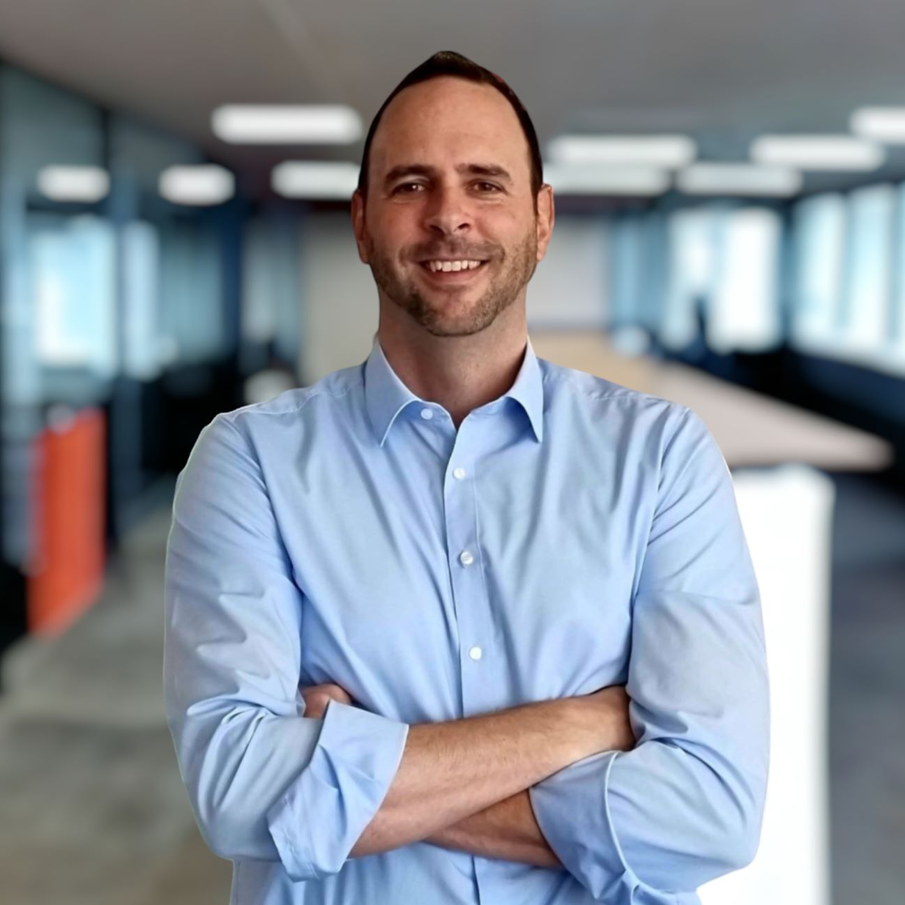 Philipp Oesch, vêtu d'une chemise bleu clair, les bras croisés, sourit à la caméra. En arrière-plan, on aperçoit un bureau moderne avec des cloisons en verre et un espace de réunion.